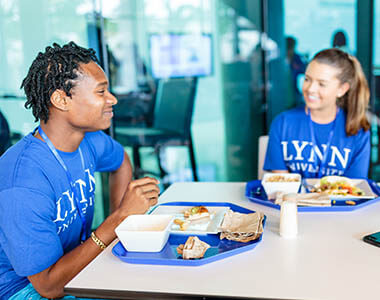 two Lynn University students in Lynn-branded t-shirts eating in a cafeteria