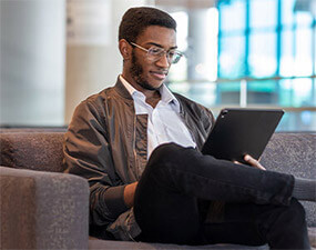 young african-american man wearing glasses sitting on a couch looking at a tablet