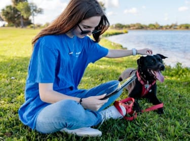 A student studies outside while sitting with her dog by a lake