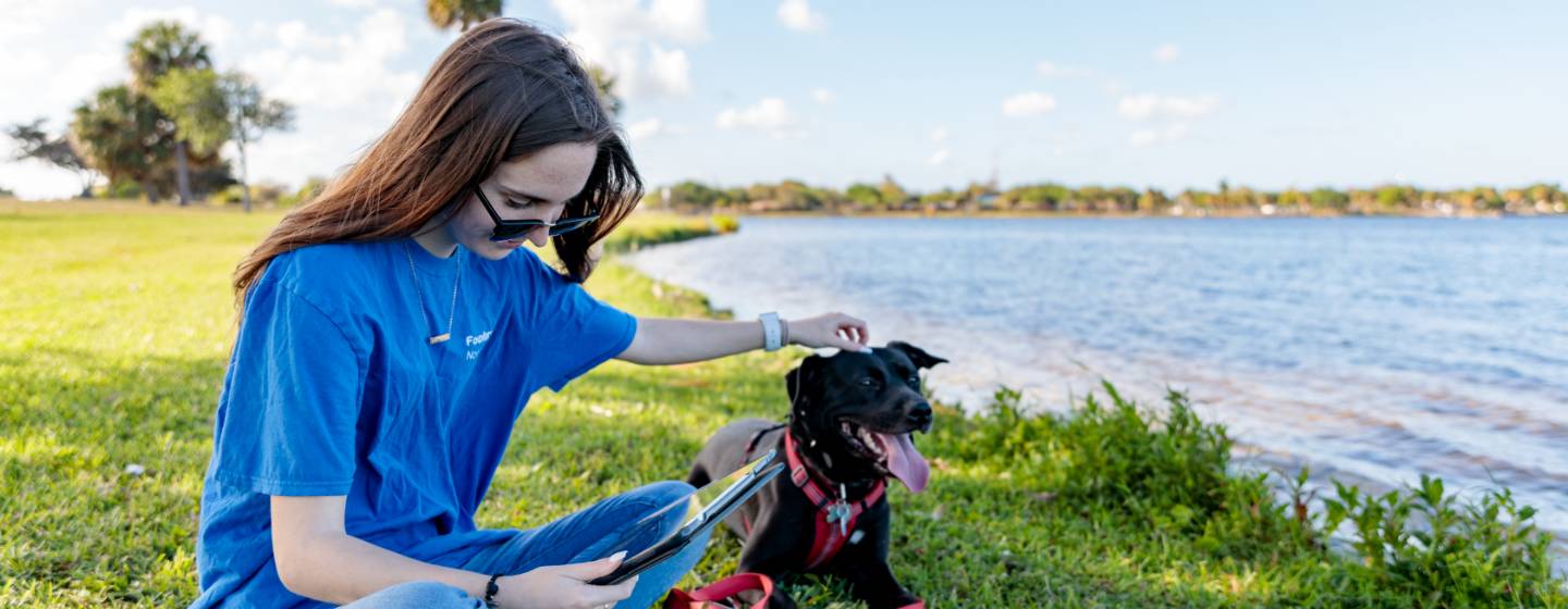 A Lynn student sits with her dog near a lake while studying